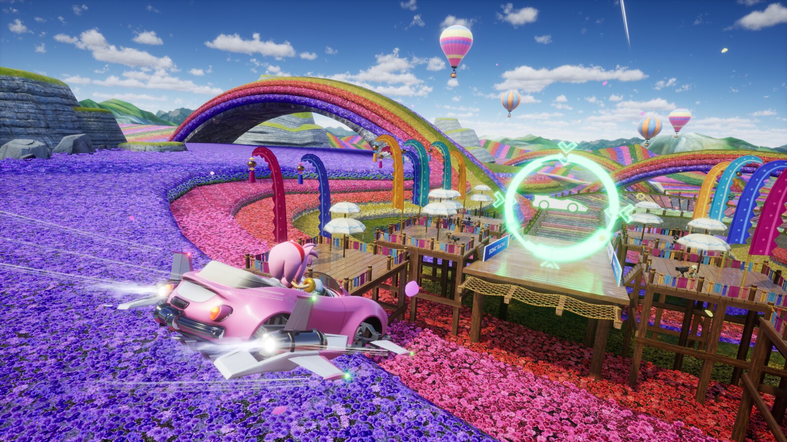 Amy soars over a purple and red field of flowers, aiming to land at a track in the distance. Her car’s wheels have converted to wings and booster rockets.

